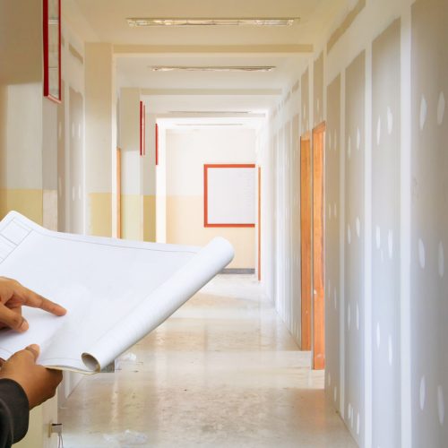 engineer finger point on paper plan blueprint in check building technician place construction site gypsum board wall interior  background